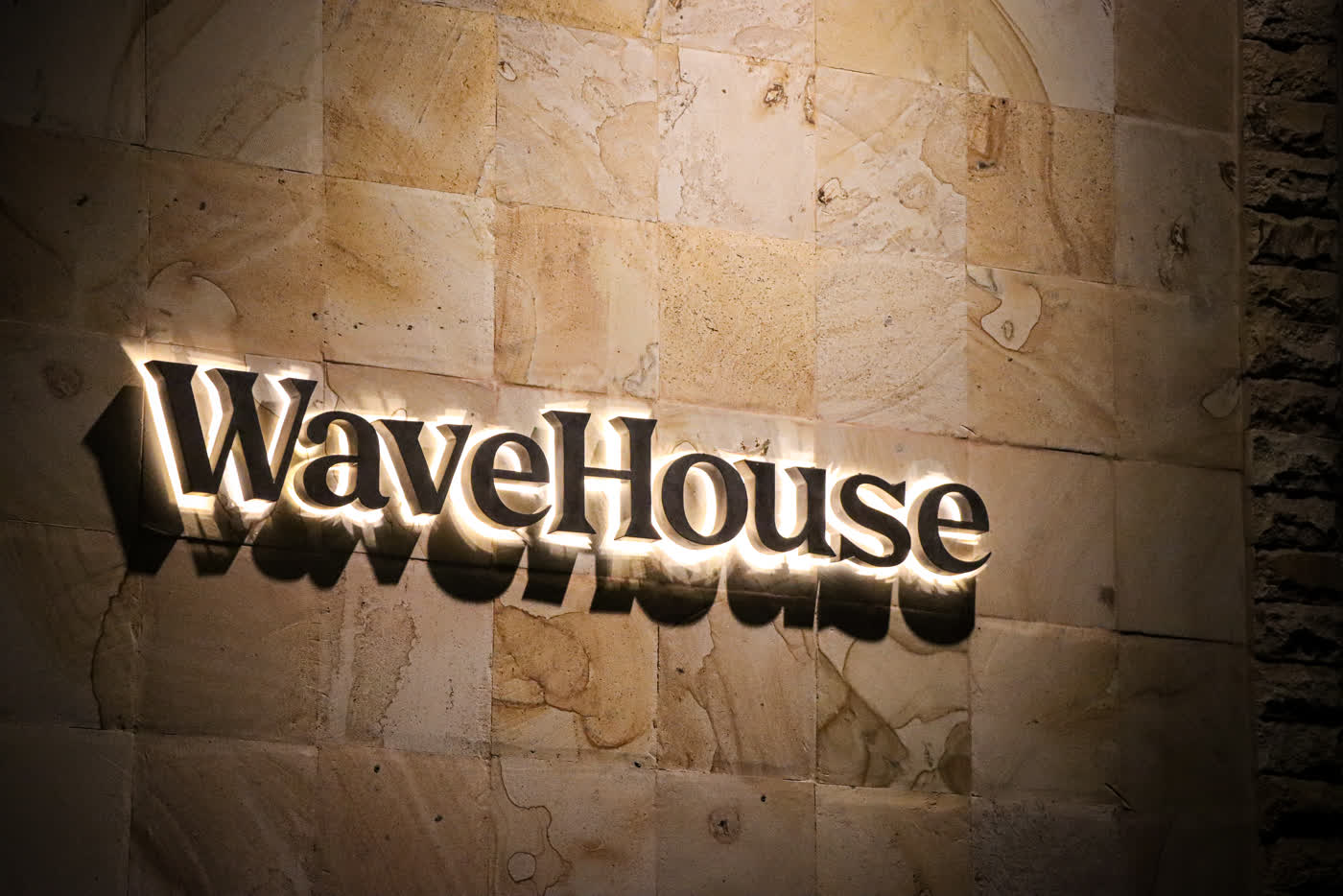 Beleuchtetes Wave-House-Logo an der Steinwand